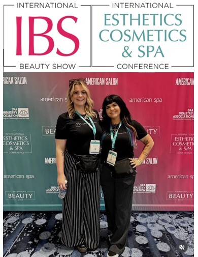 Two women posing at the International Beauty Show (IBS) and International Esthetics Cosmetics & Spa Conference with branded backdrop displaying American Salon and American Spa logos